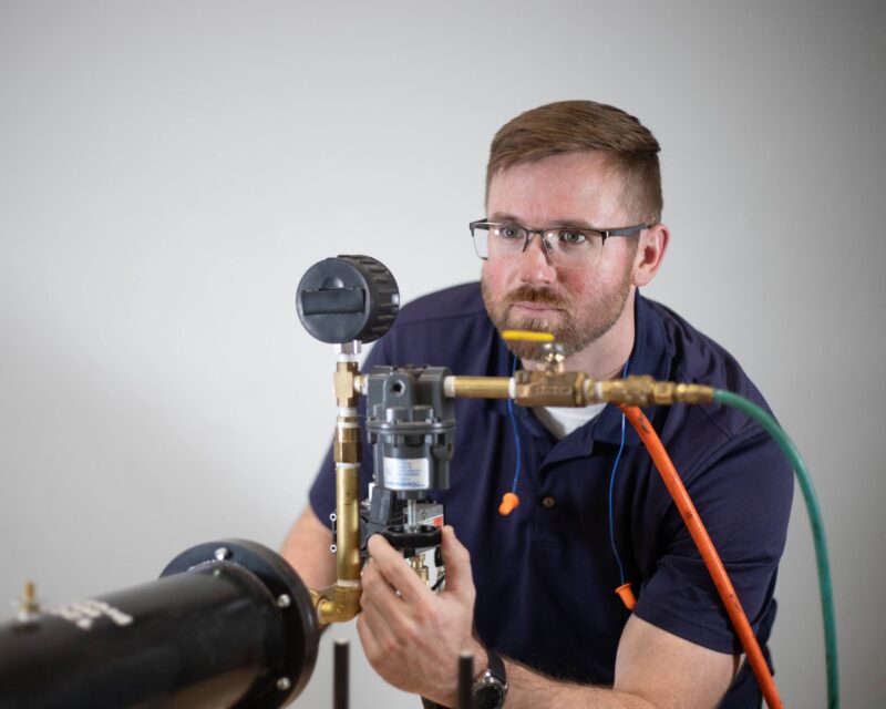 Man adjusting a pressure gauge on industrial equipment.