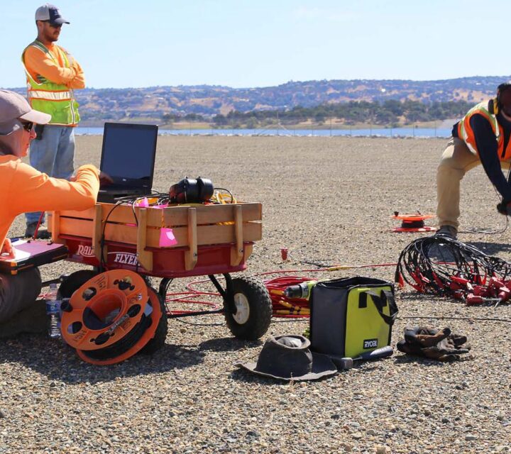 Survey crew conducting geophysical measurements in a dry, rocky field with equipment and laptops.