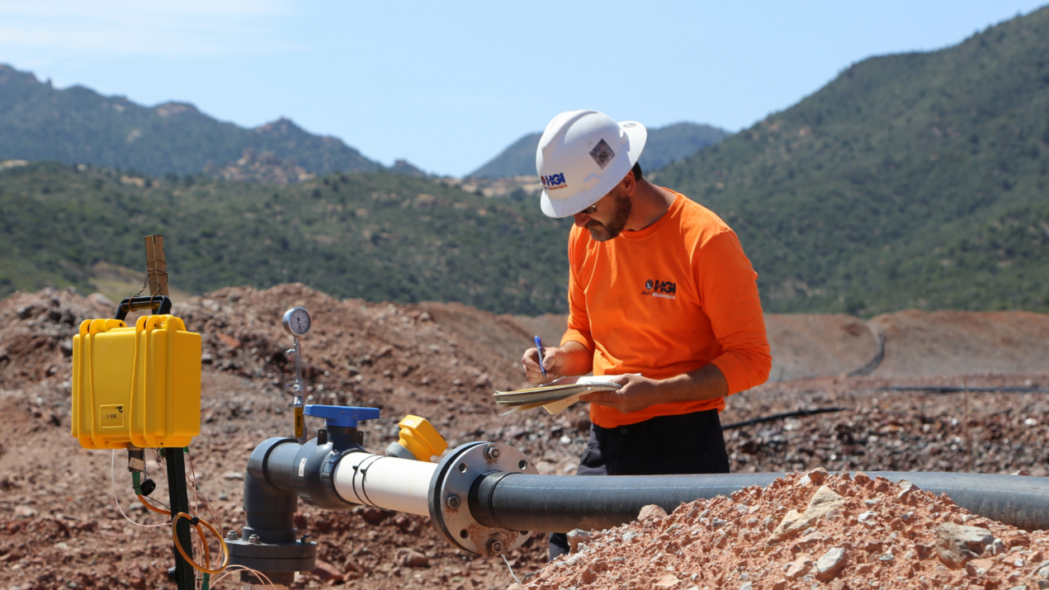Engineer inspecting pipeline in a rugged mountain landscape, taking notes on a clipboard.