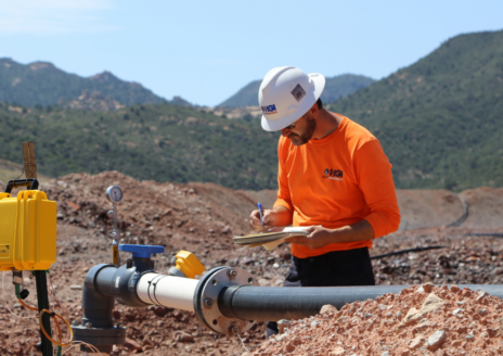 Engineer inspecting pipeline in a rugged mountain landscape, taking notes on a clipboard.