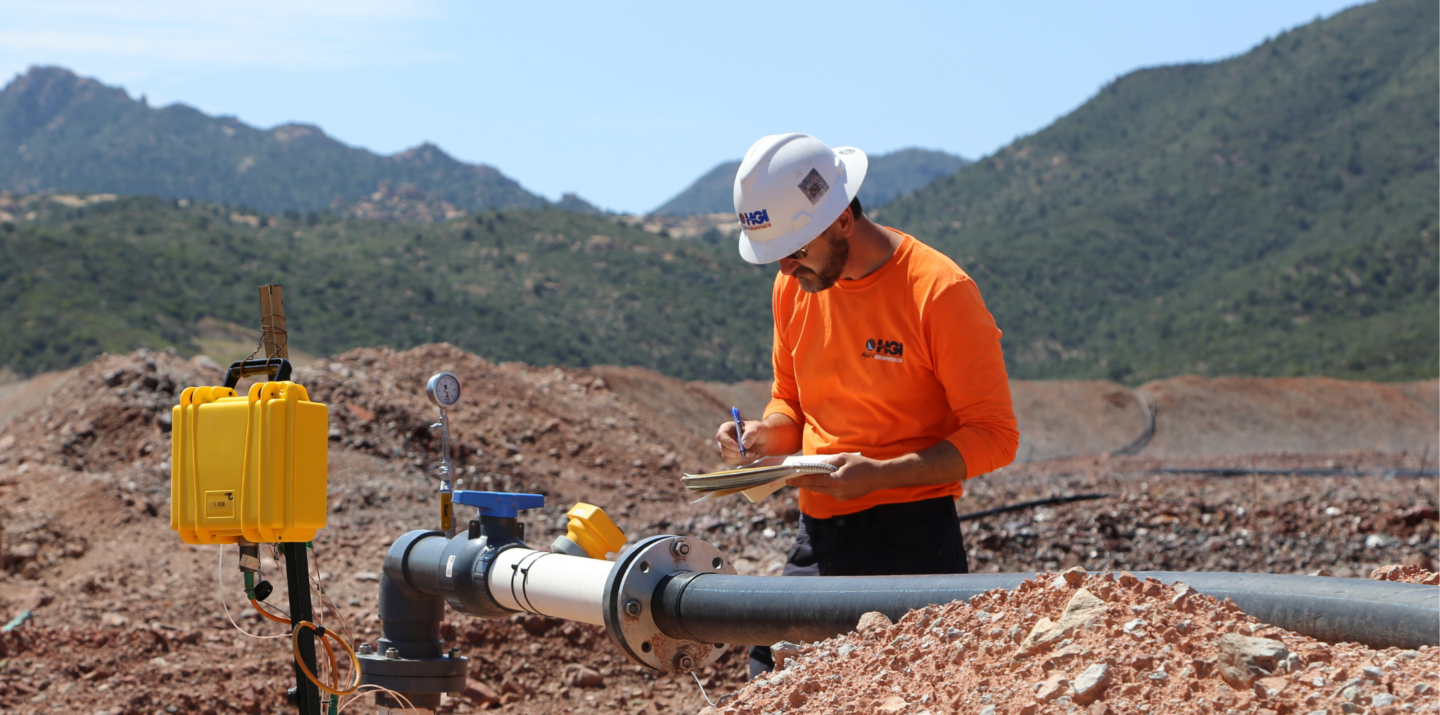 Engineer inspecting pipeline in a rugged mountain landscape, taking notes on a clipboard.