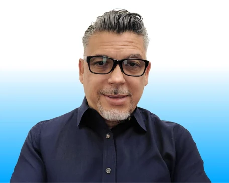 Man with dark glasses and a neatly trimmed beard, wearing a navy shirt, against a blue gradient background.