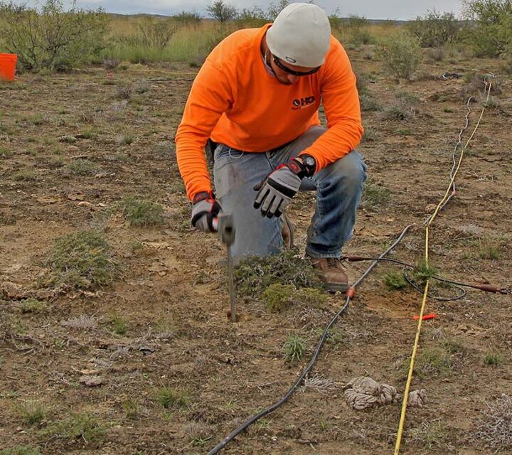 Person in orange shirt setting up markers in a dry, grassy landscape.
