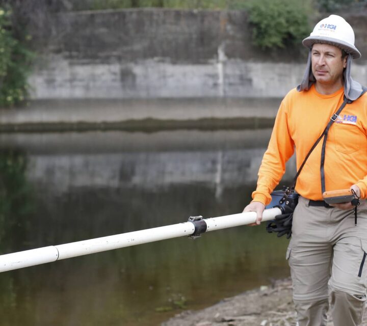Person in orange shirt carrying equipment by a water canal.