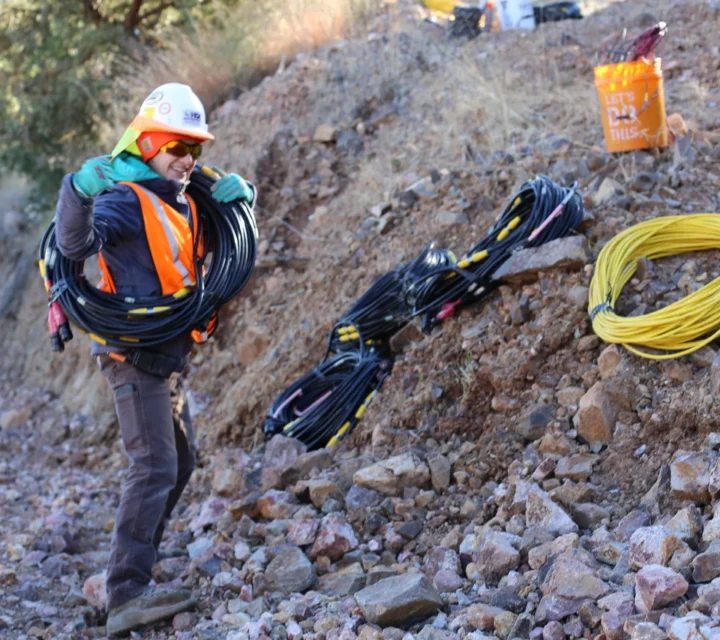 Technician carrying seismic cables during a bedrock depth mapping survey, preparing non-invasive seismic profiling equipment to define depth-to-bedrock, reduce subsurface uncertainty, and support structural stability and excavation planning decisions.