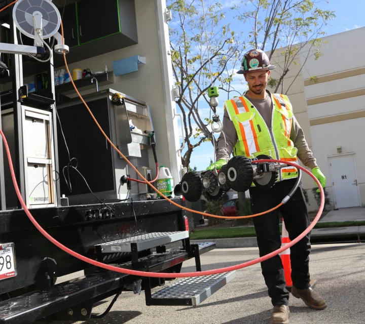 Worker in safety gear operates a remote device next to a utility truck on a sunny day.
