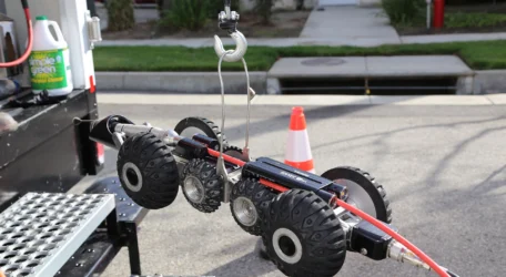 Pipe inspection robot with wheels and camera on a hook near a roadside.