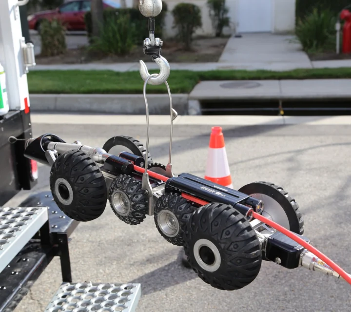 Pipe inspection robot with wheels and camera on a hook near a roadside.