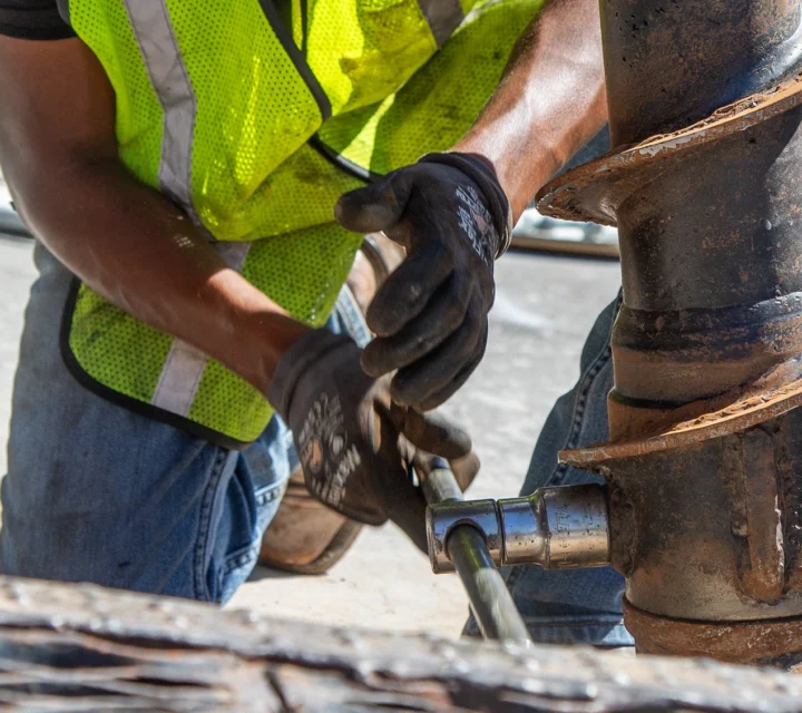 Worker in safety vest operates a large drill on a construction site.