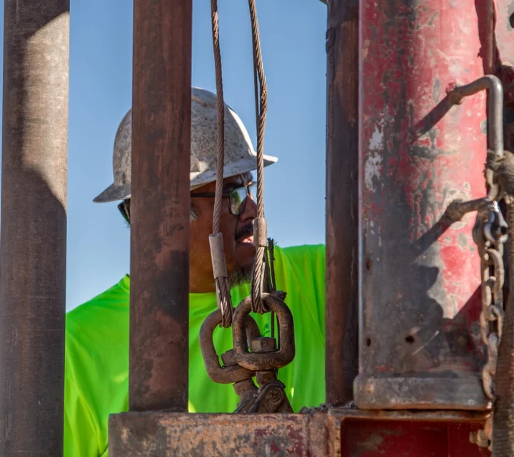 Worker in safety gear maneuvering equipment at a construction site.