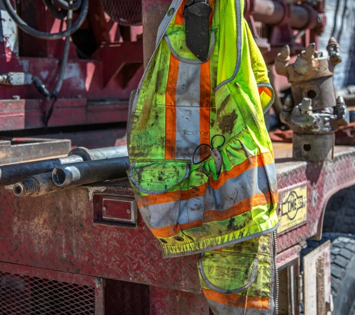 Dirty safety vest hangs on red industrial machinery outdoors.