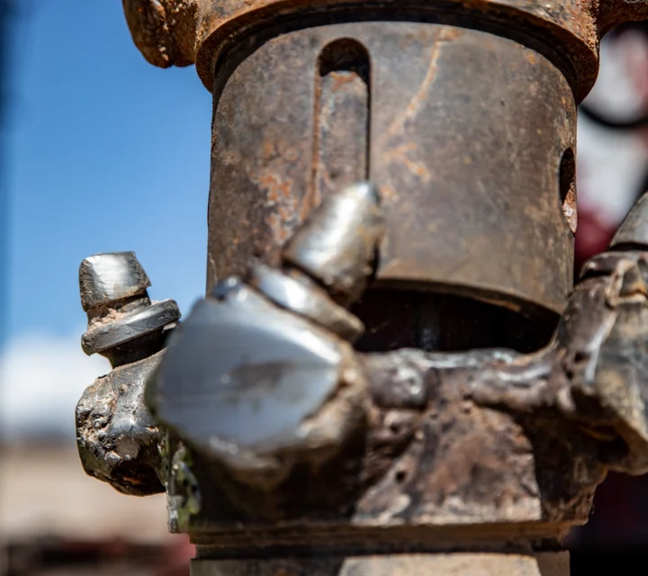 Close-up of a rusty, worn industrial tool with metal teeth, set outdoors against a blurred background.