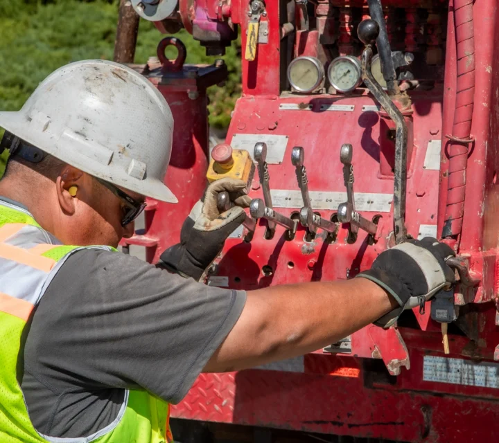 Construction worker operating machinery with control levers and gauges.