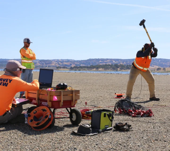 Survey crew conducting geophysical testing for dam leak detection using electrical and seismic methods to evaluate internal structure and seepage zones.
