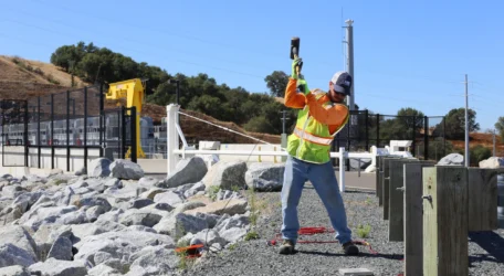 Worker in a safety vest uses a sledgehammer on rocks near construction site.