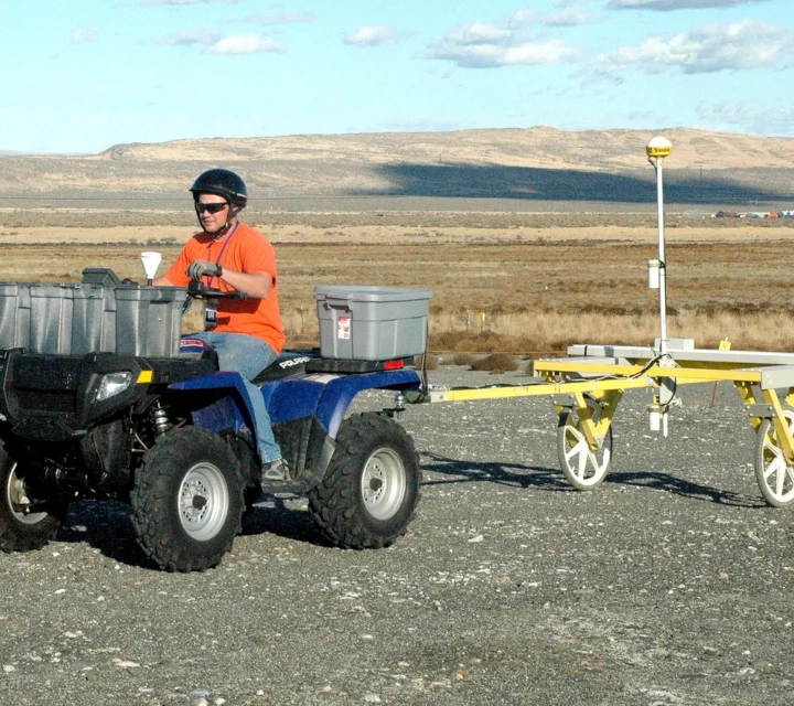 Field technician operating ATV-towed electromagnetic induction survey system collecting conductivity data across open terrain to support subsurface characterization, mapping, and planning for projects using electromagnetic induction methods.