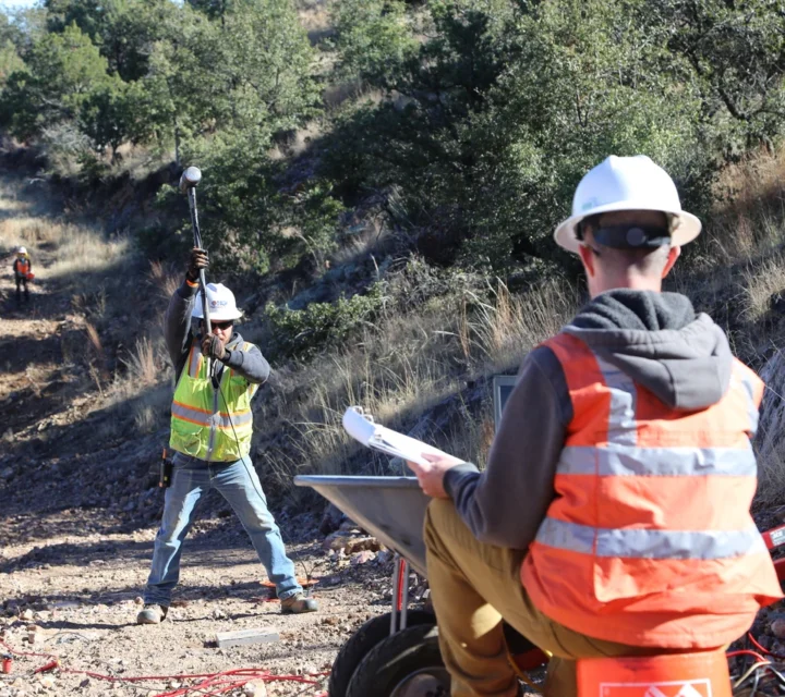 Construction workers with safety gear setting up equipment on a rocky path.