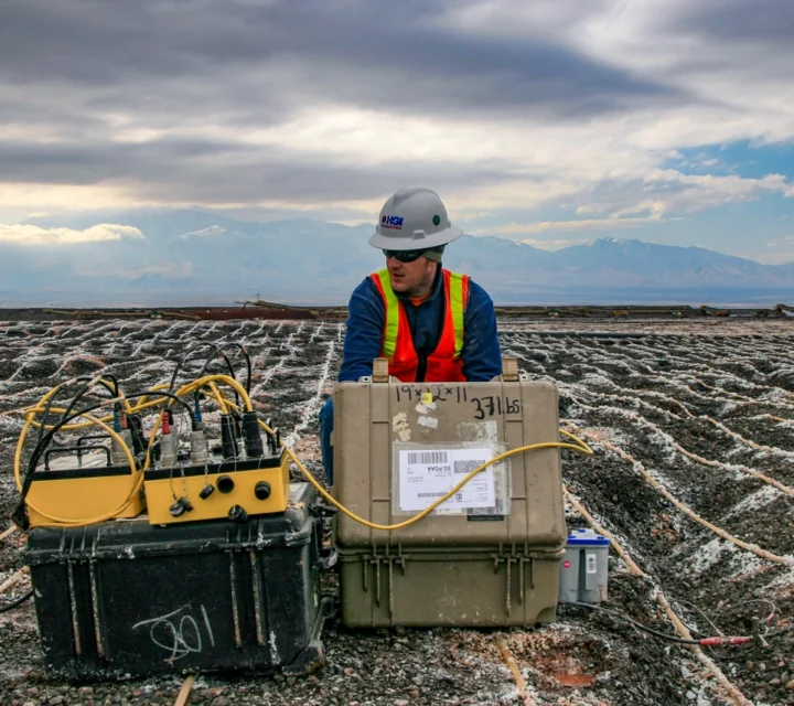 Worker in safety gear operates equipment at a construction site with a mountainous backdrop.