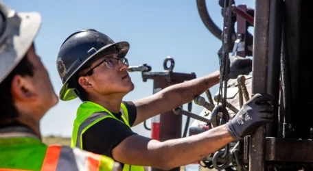 Workers in safety gear operate equipment at a construction site.