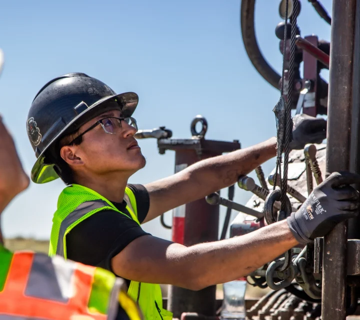 Workers in safety gear operate equipment at a construction site.