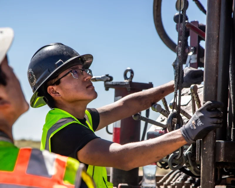Workers in safety gear operate equipment at a construction site.
