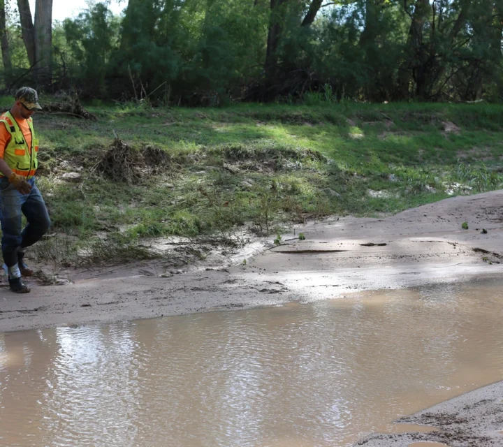 Geophysical technician conducting groundwater exploration along riverbank to evaluate groundwater and surface-water interaction, subsurface structures, basin boundaries, and flow pathways influencing groundwater storage and contaminant transport.