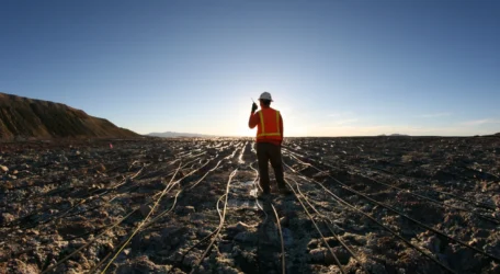 Technician walks across heap leach pad deploying survey cables for Heap leach characterization, collecting geophysical data on moisture distribution, flow pathways, and internal structural variability within engineered rock piles.