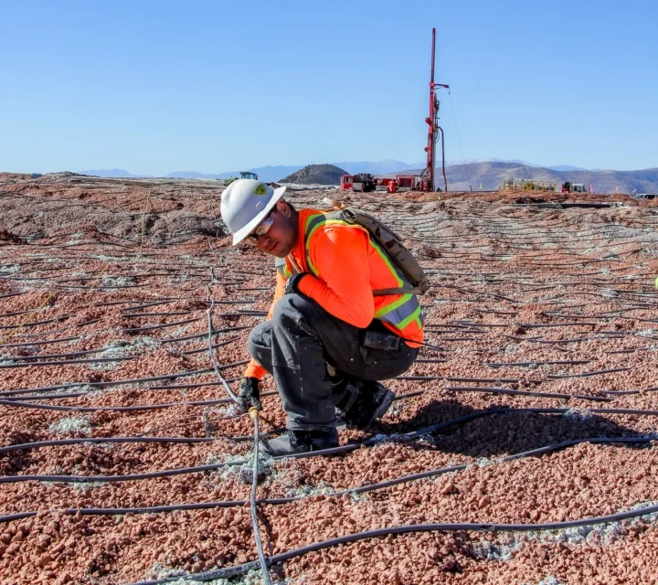 Field technician installing electrodes across heap leach pad for induced polarization survey, collecting chargeability data to characterize geochemical variability, fluid pathways, and mineralization patterns within engineered mining materials and subsurface structures.