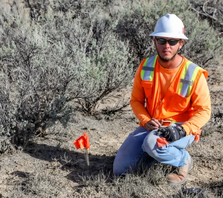 Field technician placing electrode marker during induced polarization survey in semi-arid terrain, collecting chargeability data to identify oxidation zones, ionic variations, and subsurface fluid pathways within waste rock or tailings materials.