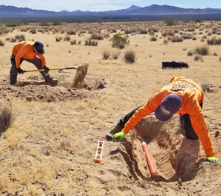 Field crew installing electrodes and magnetic sensors in desert terrain for magnetotellurics survey to measure natural electromagnetic fields and image deep subsurface resistivity for regional characterization and exploration studies.