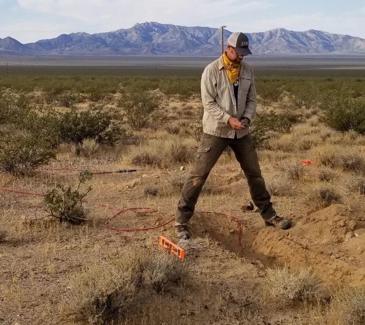 Trench with electrode and cable installed in desert soil for magnetotellurics survey measuring natural electromagnetic fields to evaluate subsurface resistivity contrasts, groundwater conditions, and geologic structure at depth.