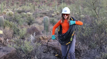 Technician carries geophysical survey cable through rugged terrain during Mineral exploration, supporting subsurface mapping of structures, boundaries, and anomalies to guide drilling priorities and reduce exploration uncertainty.