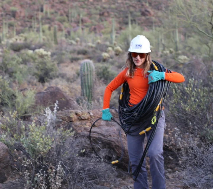 Technician carries geophysical survey cable through rugged terrain during Mineral exploration, supporting subsurface mapping of structures, boundaries, and anomalies to guide drilling priorities and reduce exploration uncertainty.