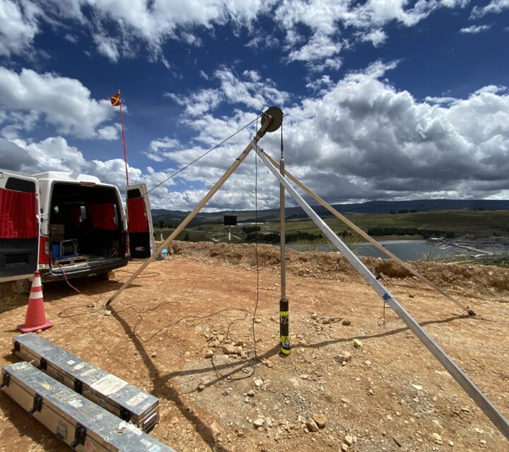 Geological survey setup with tripod and equipment near a van on a rocky terrain under a cloudy sky.