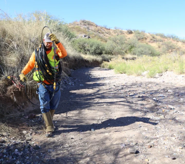 Technician deploying geophysical cables in desert terrain for plume mapping survey, supporting subsurface contamination delineation, groundwater monitoring, and environmental remediation planning through non-invasive geophysical investigation methods.