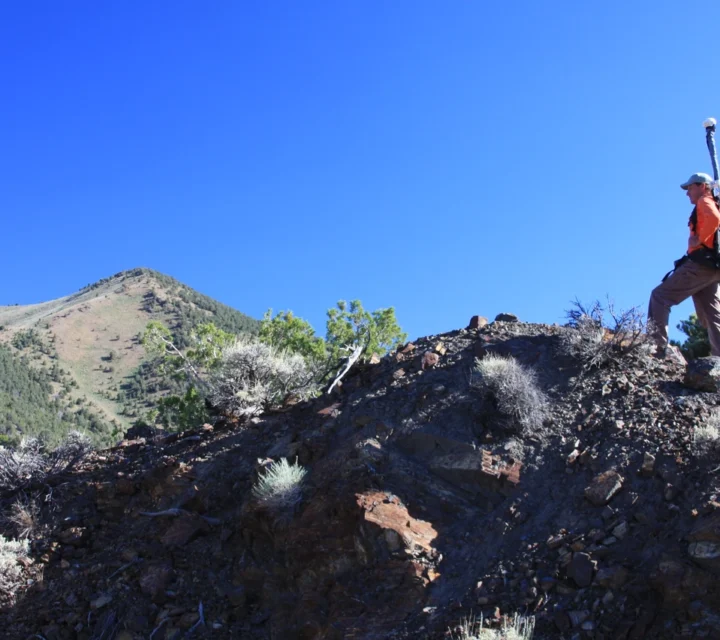 Person hiking on rocky terrain with hiking poles under a clear blue sky.