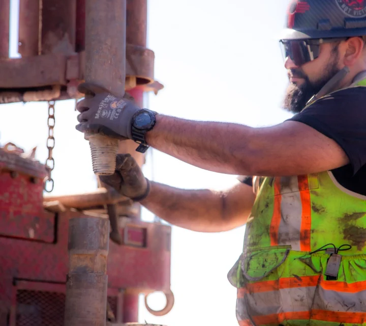 Construction worker in safety gear handling drilling equipment outdoors.