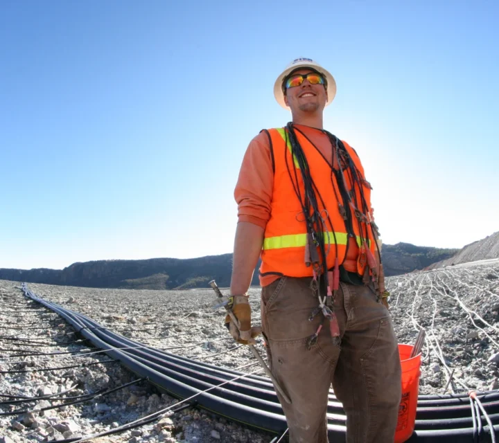 Technician stands on mining facility with survey cables during Seepage and ARD mapping, supporting geophysical methods that identify fluid pathways, saturation patterns, and abnormal seepage conditions within engineered materials.