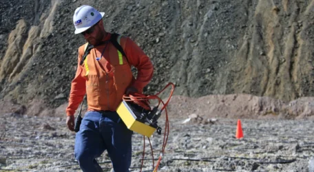Technician carries geophysical instrument across mine surface during Seepage and ARD mapping, collecting subsurface data to identify preferential flow paths, saturation zones, and conditions linked to acid rock drainage.