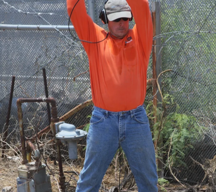 Technician generating controlled surface energy with sledgehammer for seismic refraction survey while sensors record wave arrivals to estimate subsurface velocities, layer boundaries, and material contrasts along profile.