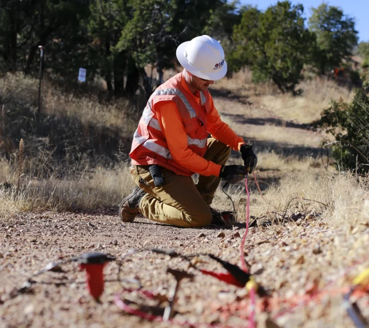 Technician installing geophones and cable for seismic refraction survey along ground surface to measure travel times and estimate subsurface layer velocities and depth to bedrock for site characterization.