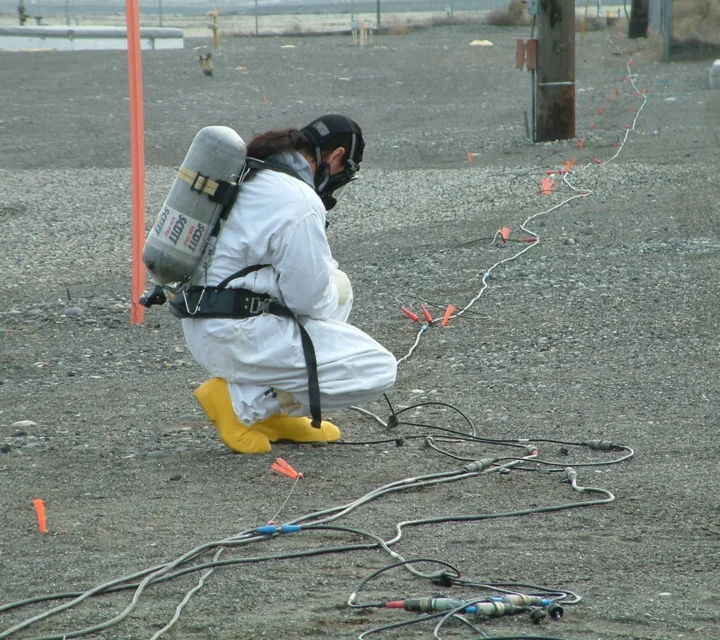 Technician in protective gear installing surface electrodes and monitoring cables during soil characterization survey to evaluate subsurface variability, contamination potential, and soil stability conditions.