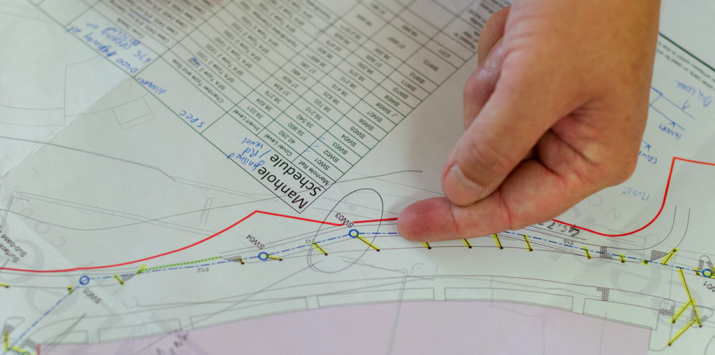 Hand pointing to a section on a technical map with marked lines and tables.