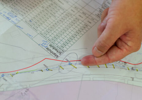 Hand pointing to a section on a technical map with marked lines and tables.