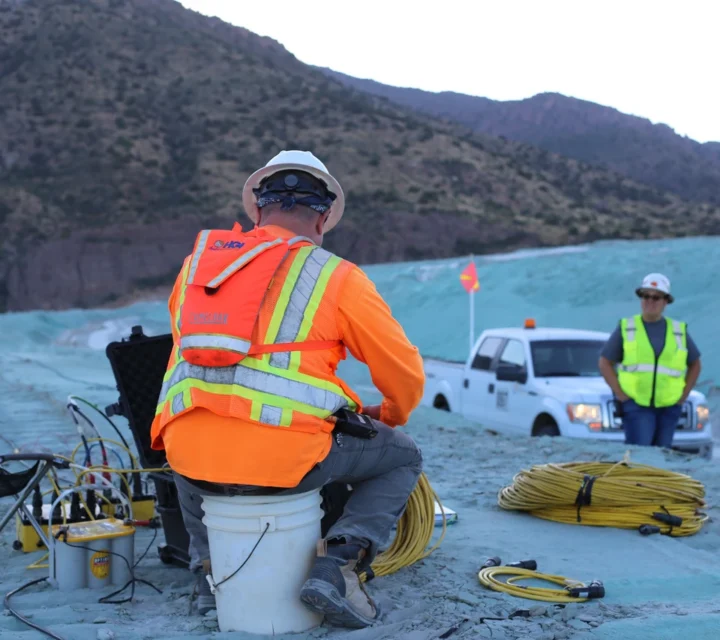 Survey crew deploys cables and instruments on tailings facility for Tailings dam characterization, collecting geophysical data to monitor saturation, solution movement, and material conditions affecting containment and environmental risk.