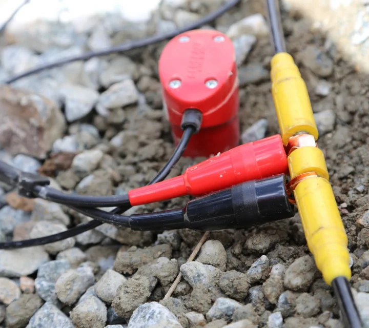 Electrical connectors and wires on rocky ground.
